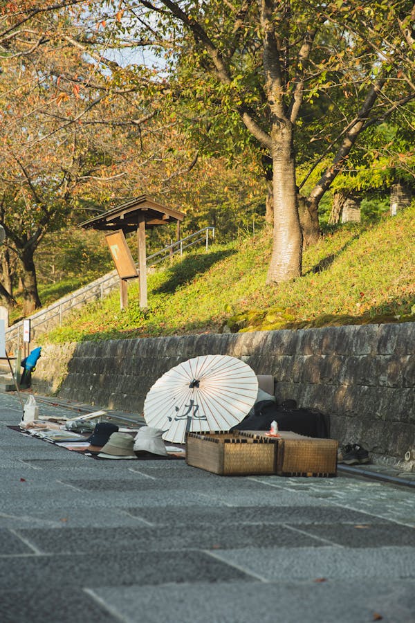 White oil paper umbrella and various traditional Asian items placed on paved walkway for sale in Kyoto on sunny day