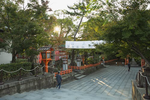 Free Unrecognizable people walking on paved pathway near green trees while sightseeing ancient Yasaka Shrine located in Kyoto Stock Photo