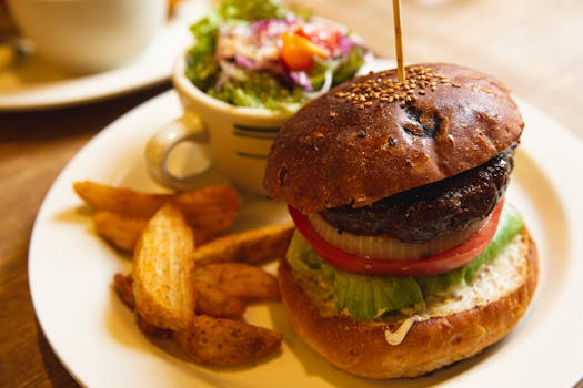 Delicious burger with fries and salad served on a white plate, offering a tempting fast food meal.