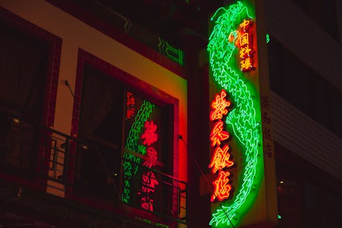 From below of bright glowing neon signboard in oriental style hanging on facade of building at night