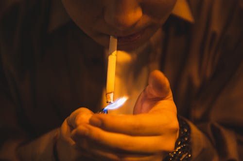 Crop male with burning lighter and cigarette smoking for reducing stress in light of lamp