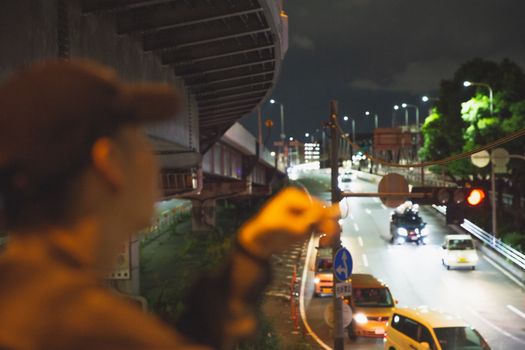 在灯光明亮的桥上，一个模糊的人影俯瞰着大阪夜间的交通