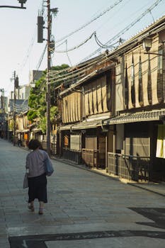 在日本京都一条宁静的街道上，一名妇女漫步经过传统的木制建筑