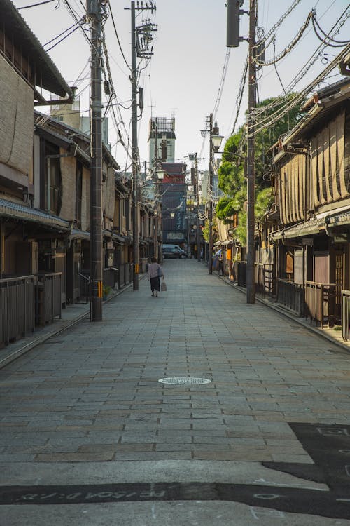 Free Back view distant unrecognizable woman strolling on paved walkway in old city district near typical small houses in Japan Stock Photo