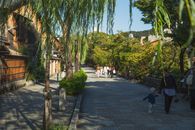 Anonymous people strolling in old city district near wooden houses and green trees