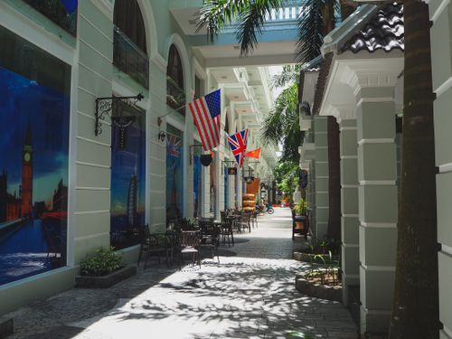 Free Narrow paved street with outdoor cafe and classic styled buildings decorated with various countries flags and banners in sunlight Stock Photo