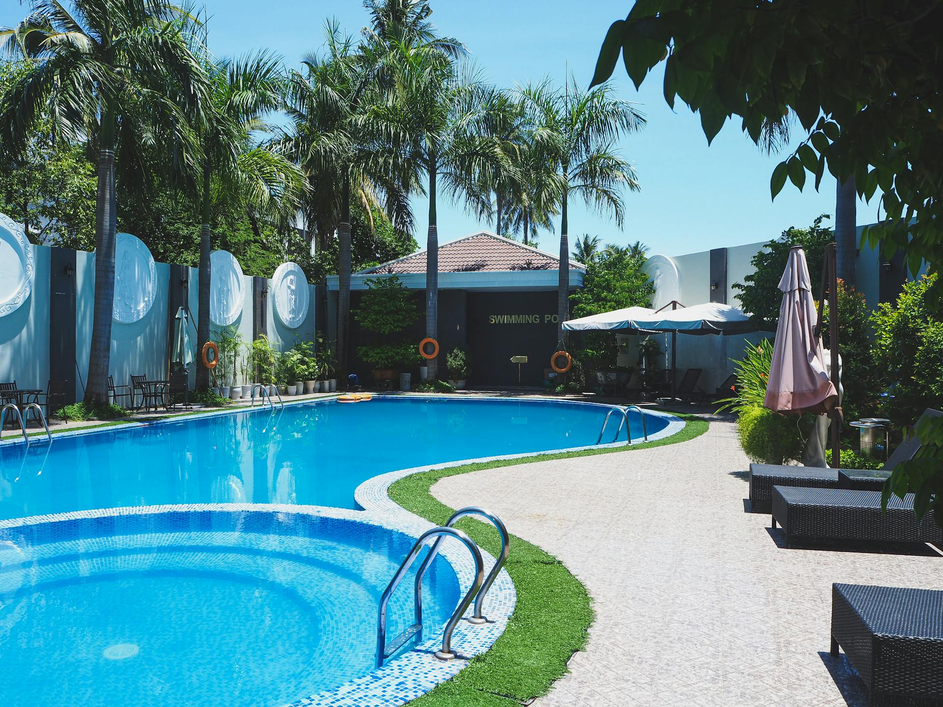 Outdoor swimming pool with sunbeds on territory of tropical hotel with green palm trees against cloudless blue sky