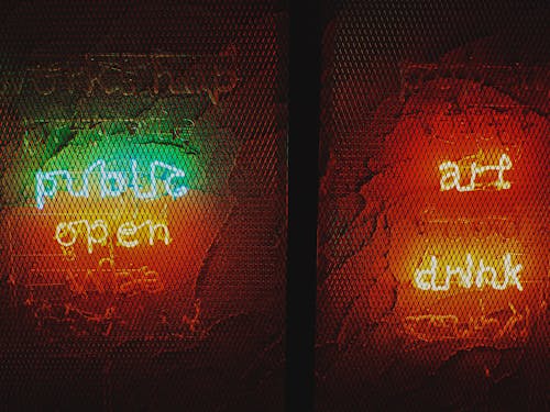 Bright glowing neon signs with various inscriptions hanging on rough wall in dark pub