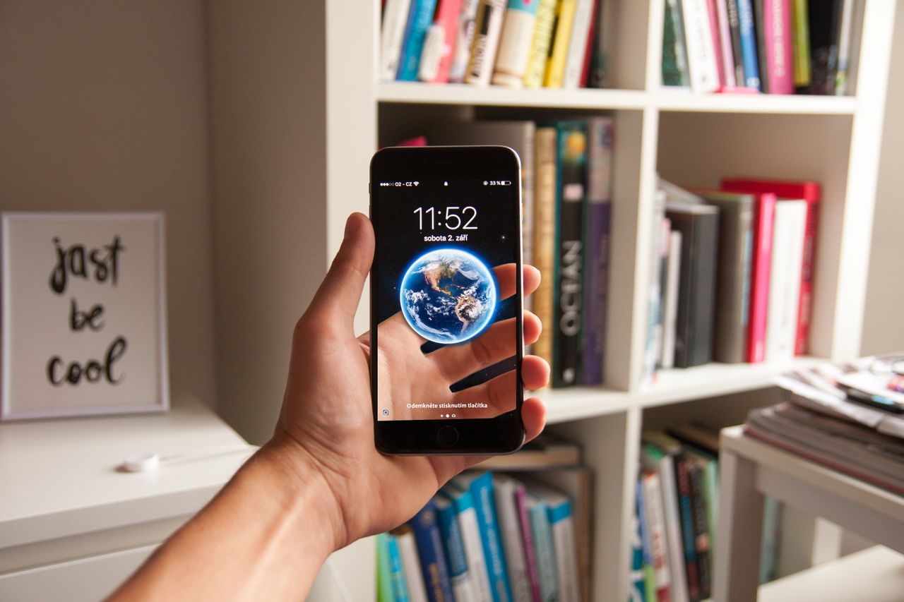 hand holding smartphone with earth wallpaper surrounded by books in a
