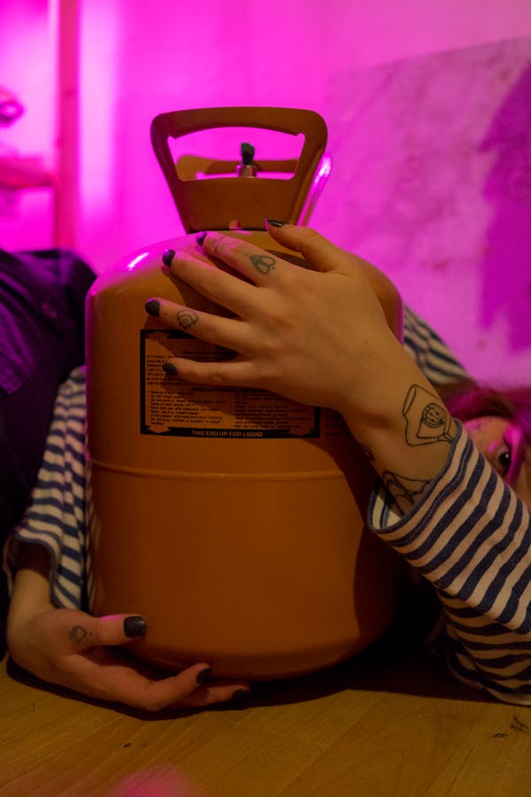 Crop faceless female with tattoos holding tank with refrigerant in room with vivid neon light
