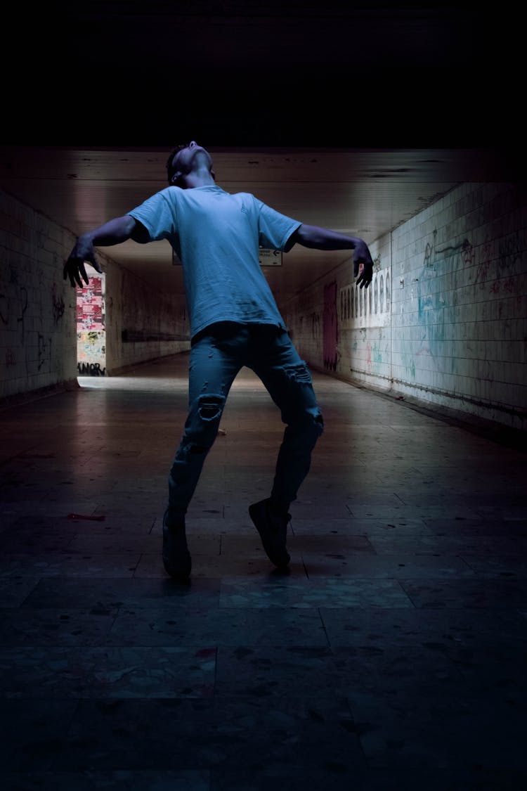 A Man In White Shirt And Ripped Jeans Dancing In A Dark Hallway