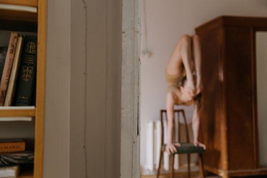 一名年轻女子在室内椅子上倒立，展现了她的平衡性和灵活性