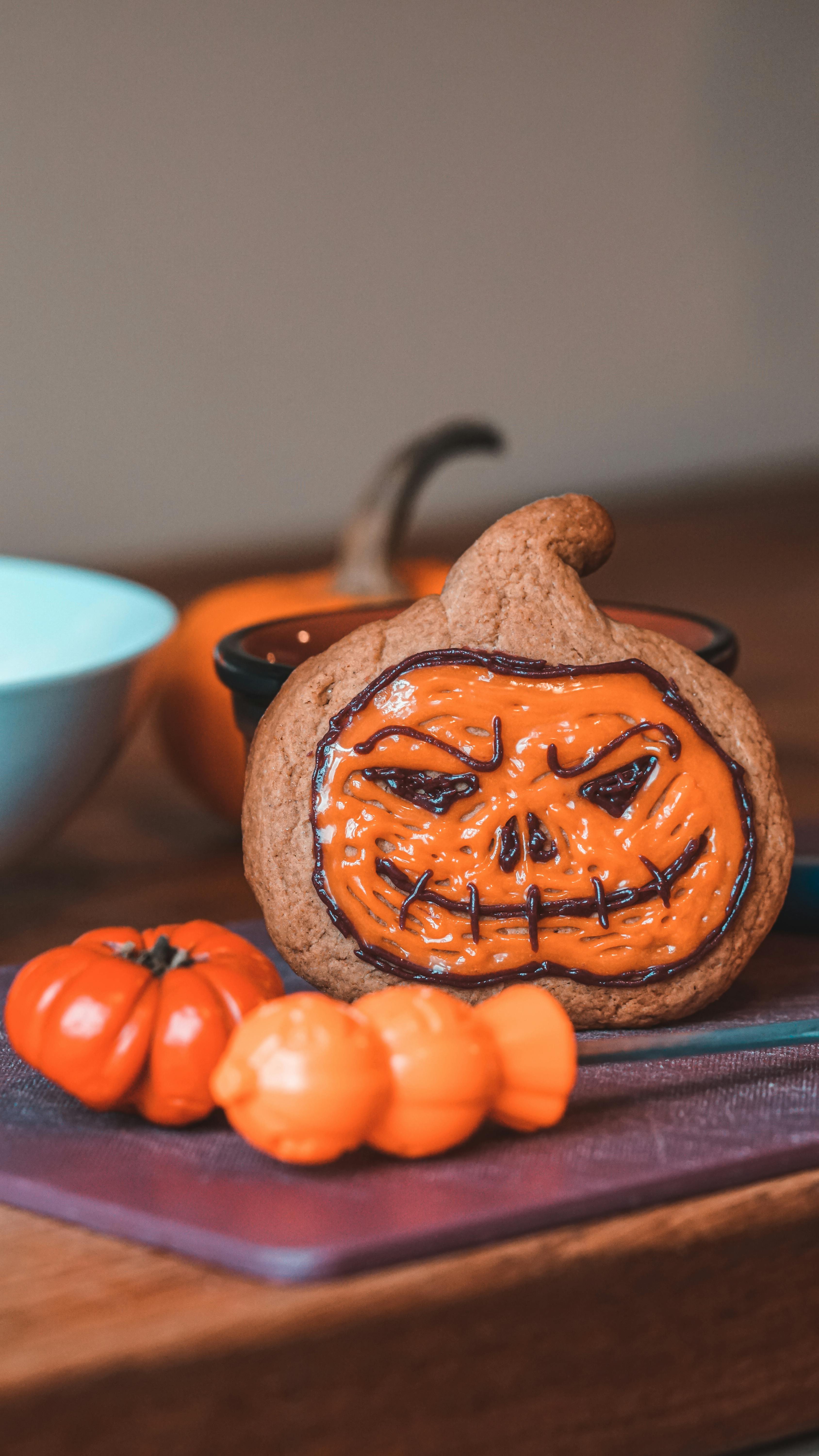 Close-up of a Halloween-themed pumpkin cookie with orange frosting on a wooden table, perfect for seasonal celebrations.