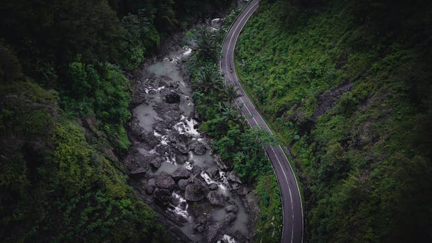 Aerial view of a winding road and river in lush jungle greenery in Central Java, Indonesia.
