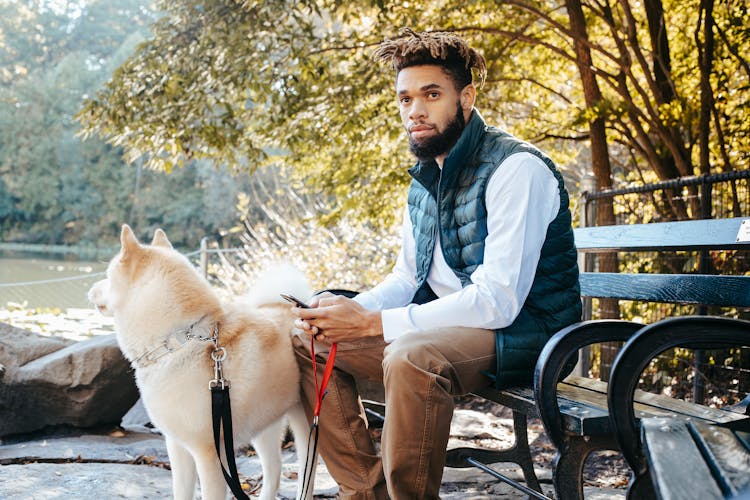 Calm Black Man With Dog Browsing Smartphone In Park