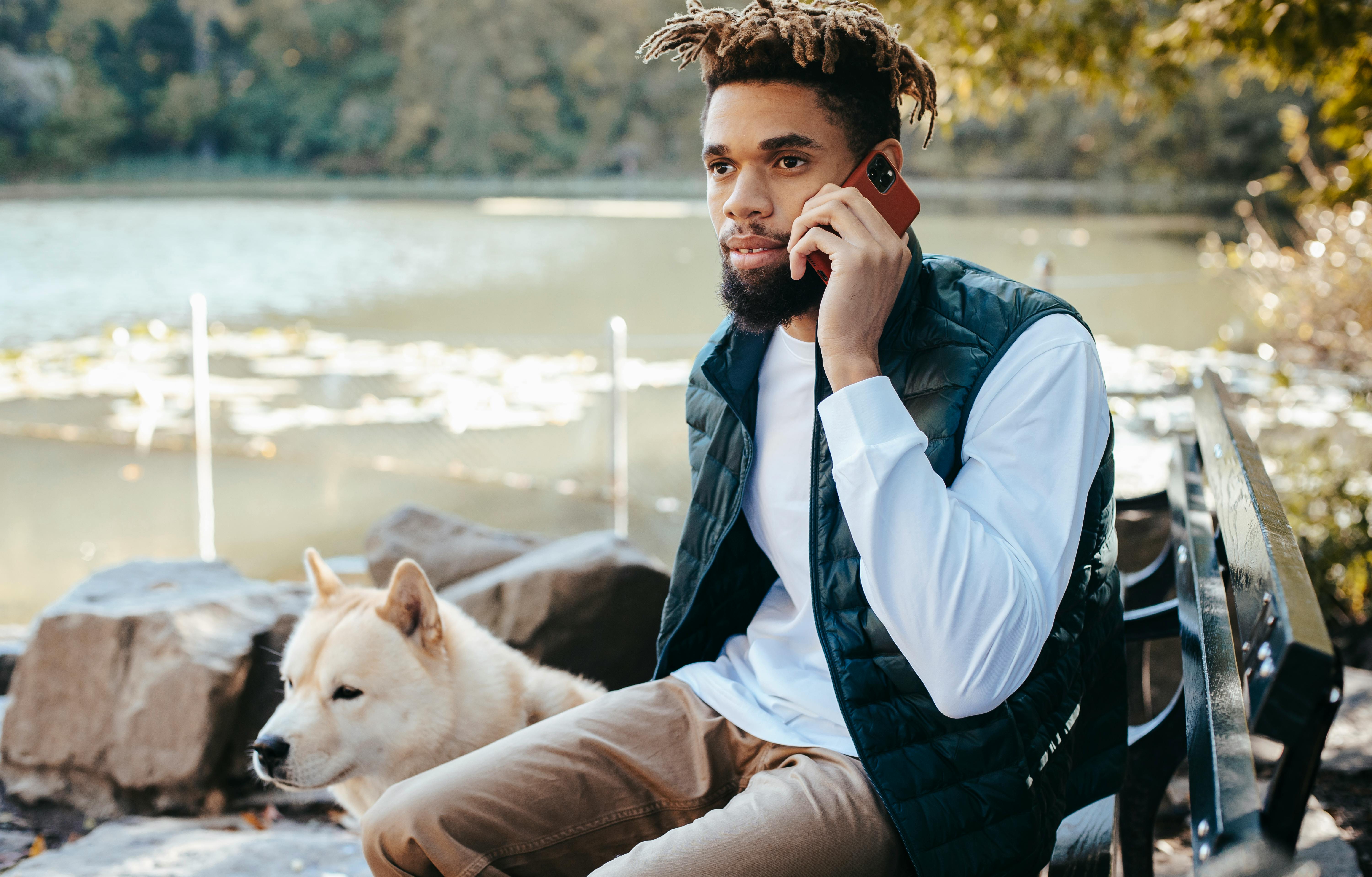 concentrated black man having conversation on smartphone near dog at pond