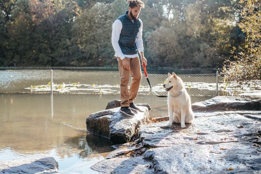 秋日阳光明媚，一名男子和他的秋田犬在平静的河边享受时光
