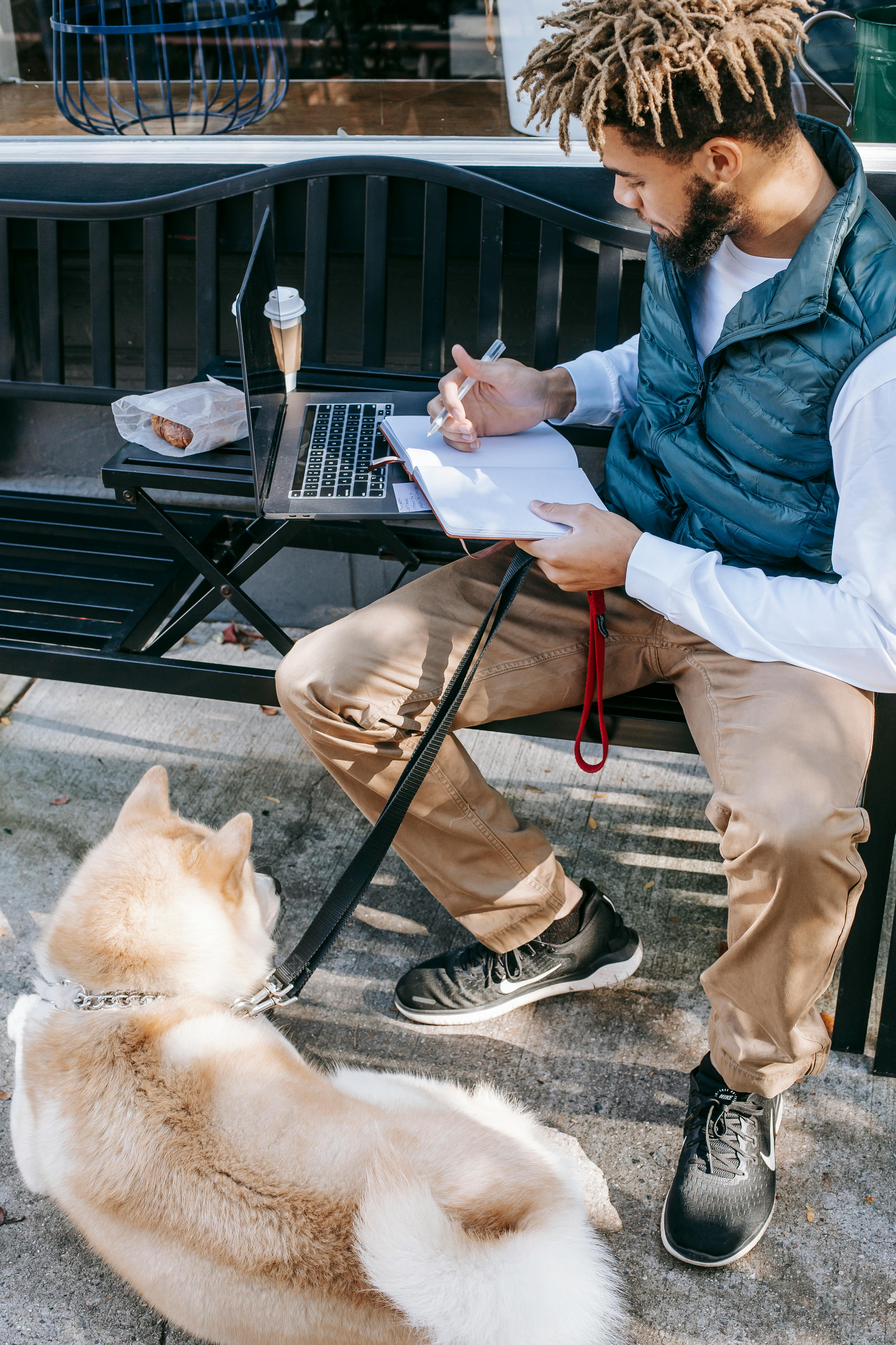 Black man writing in notepad while working near dog