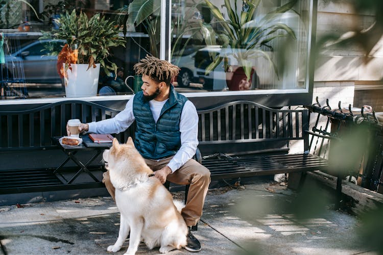 Serious Black Man With Coffee On Bench Near Dog