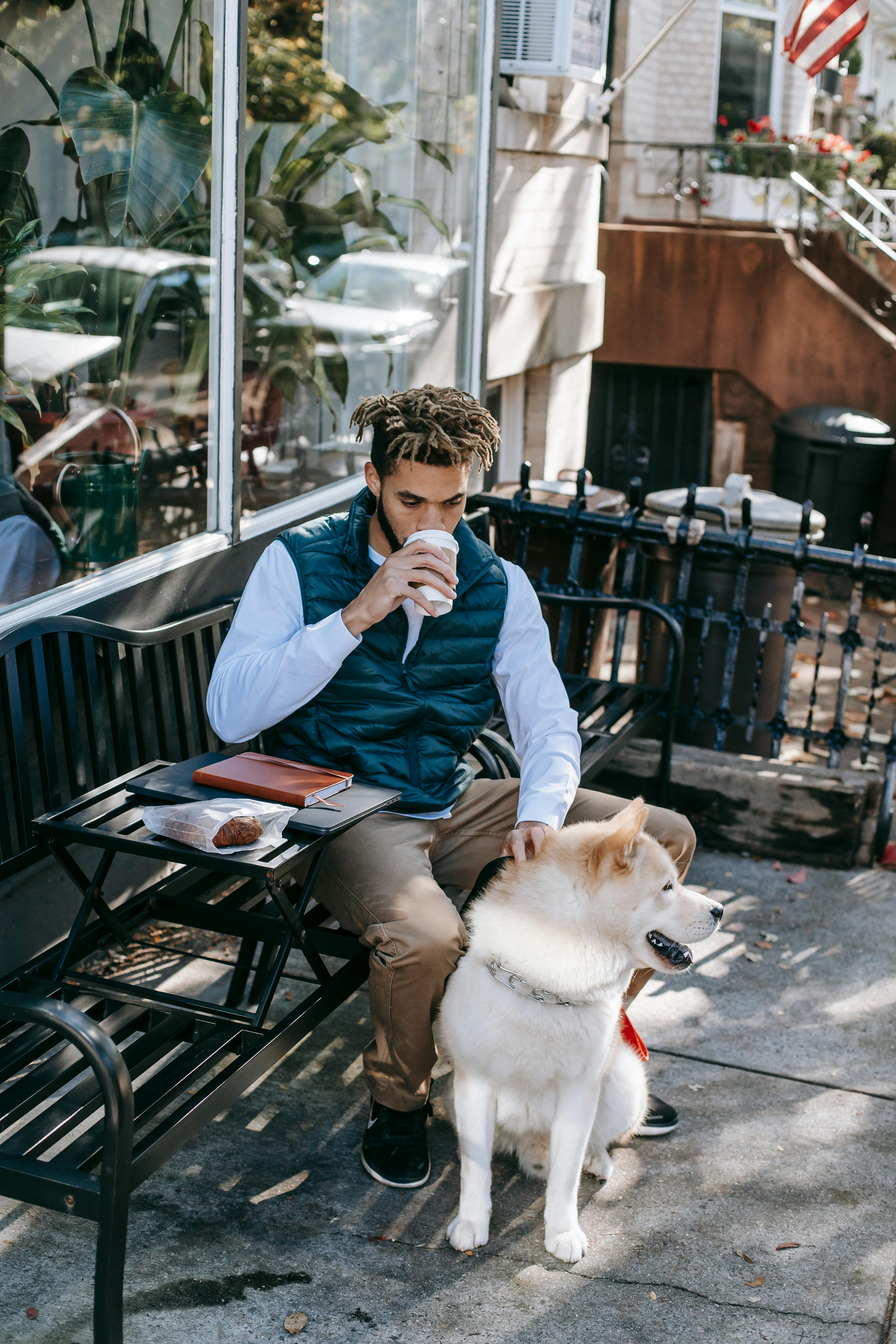 black man with dog drinking coffee on street