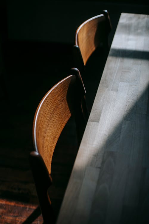 Free From above fragment of table with wooden chairs placed on lumber floor under bright sunlight in light room at home Stock Photo