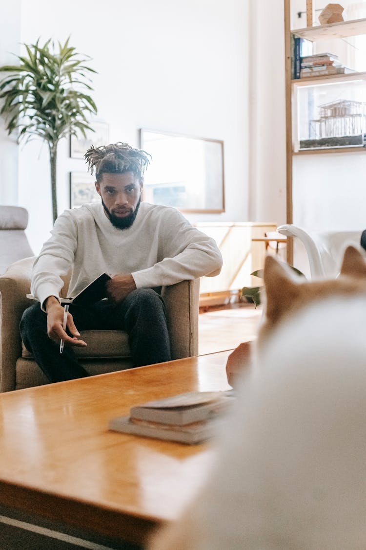 Black Man Sitting In Armchair Looking At Dog In Room