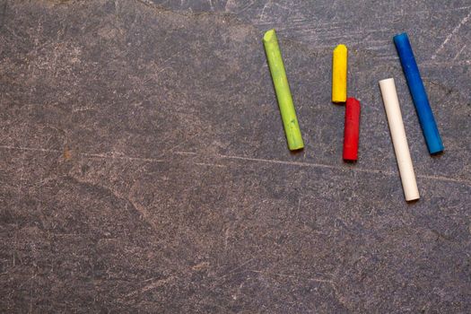 Top view set of multicolored round chalks for drawing scattered on dark shabby surface with painted lines in modern studio