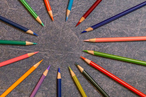 Top view set of multicolored wooden pencils with sharp tips arranged in form of circle on dark table in studio