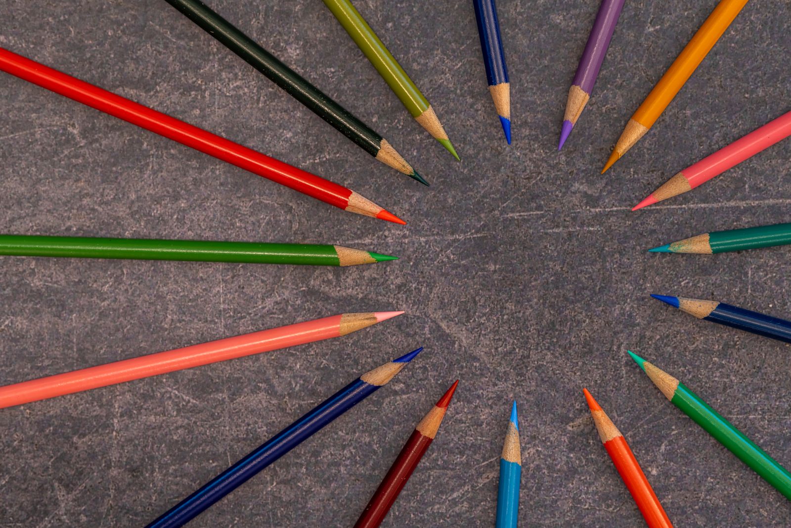 Dozens of colored pencils arranged in a bright radial rainbow pattern