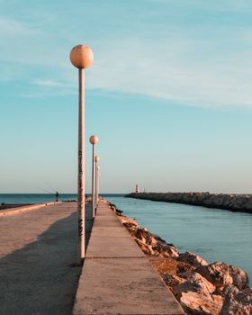 A tranquil view of Quarteira's promenade with light posts and the ocean under a blue sky.