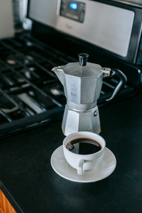 Free From above of cup of fresh brewed coffee cup placed on table with moka pot near stove in kitchen Stock Photo