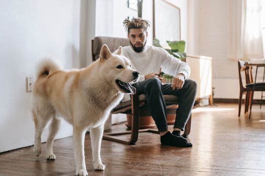 在明亮舒适的客厅里，一个年轻人和他的秋田犬坐在扶手椅上