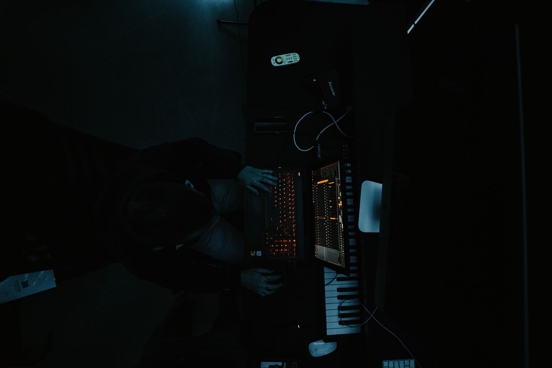 Overhead view of a person at a backlit keyboard and screen in a dark room