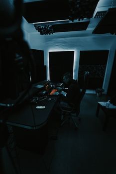 A music producer focused on a project in a dimly lit professional recording studio.