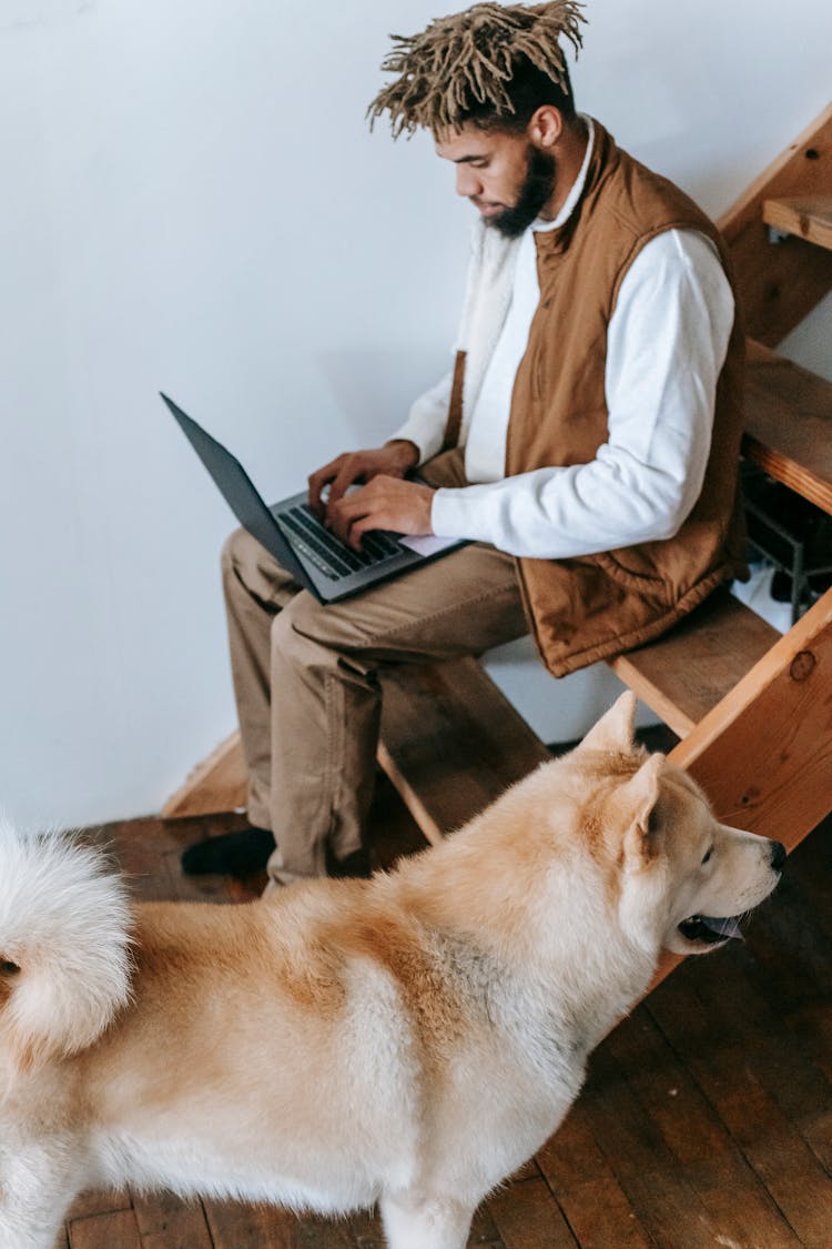 African American Guy Sitting On Stairs With Netbook Near Dog