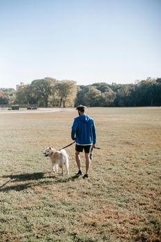 晴朗的蓝天下，一位身着运动服的无脸男子带着秋田犬在草地上散步