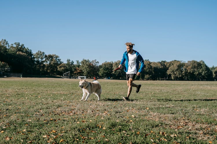 Happy Man Running With Dog In Park