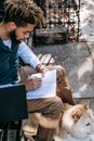 年轻人在户外用笔记本写作，秋田犬在他身边