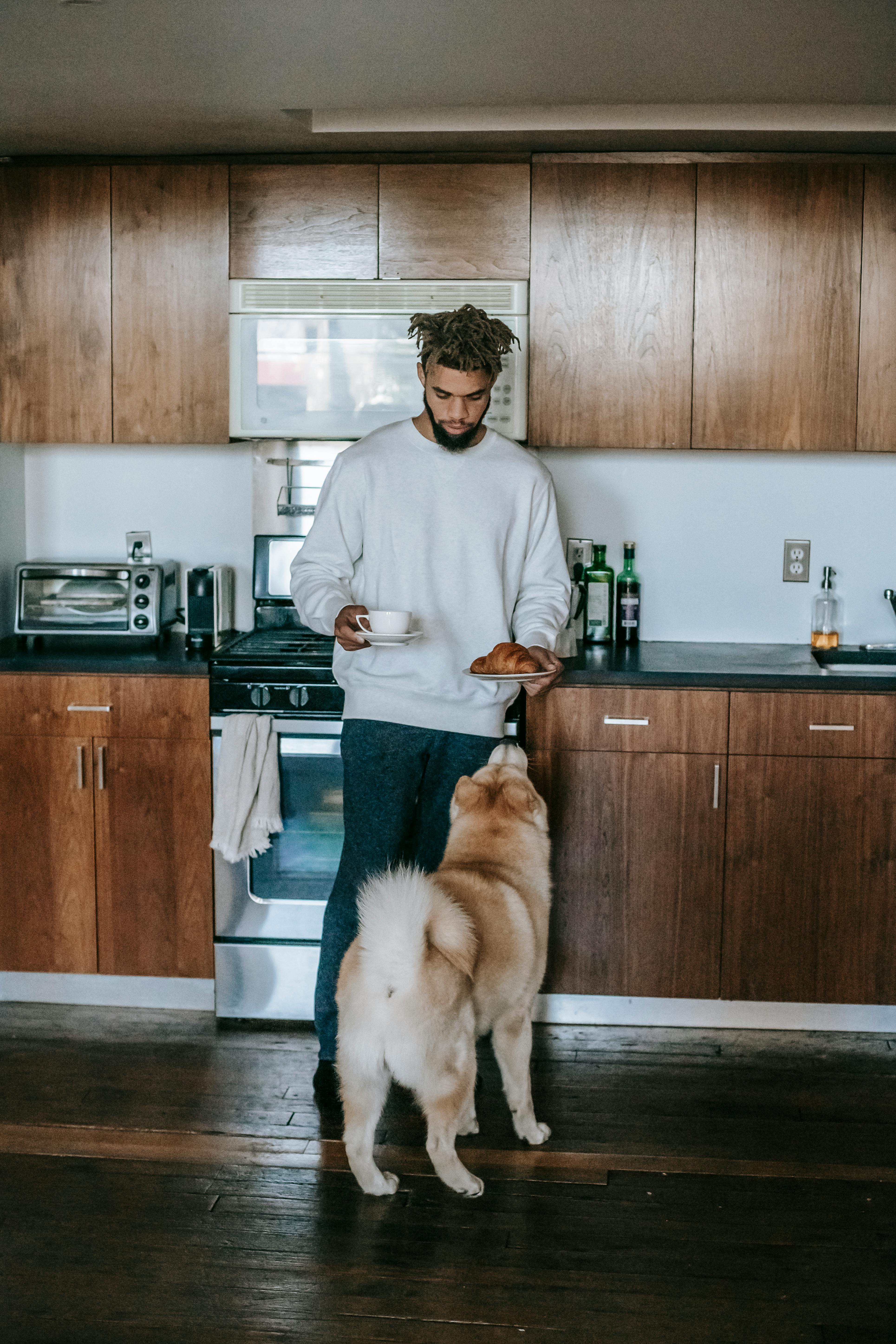 black man standing with cup of coffee and croissant near akita inu