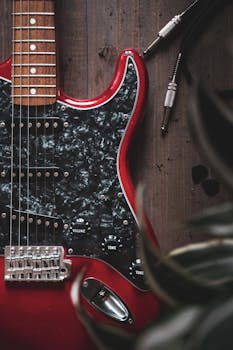Detailed view of a red electric guitar on a wooden surface with cables and black knobs.