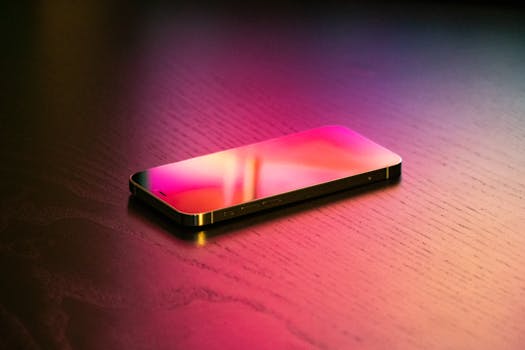 Close-up of a smartphone displaying colorful reflections on a wooden surface, captured in a studio.