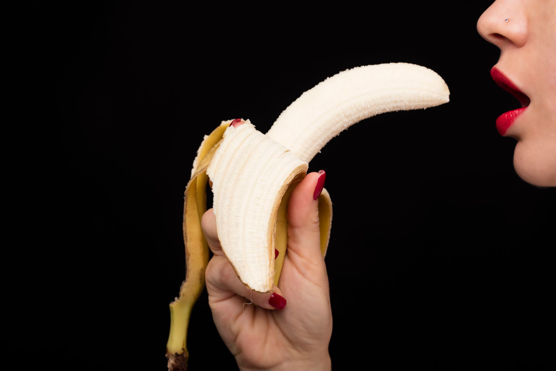 Artistic image of a person holding a half-peeled banana against a black background.