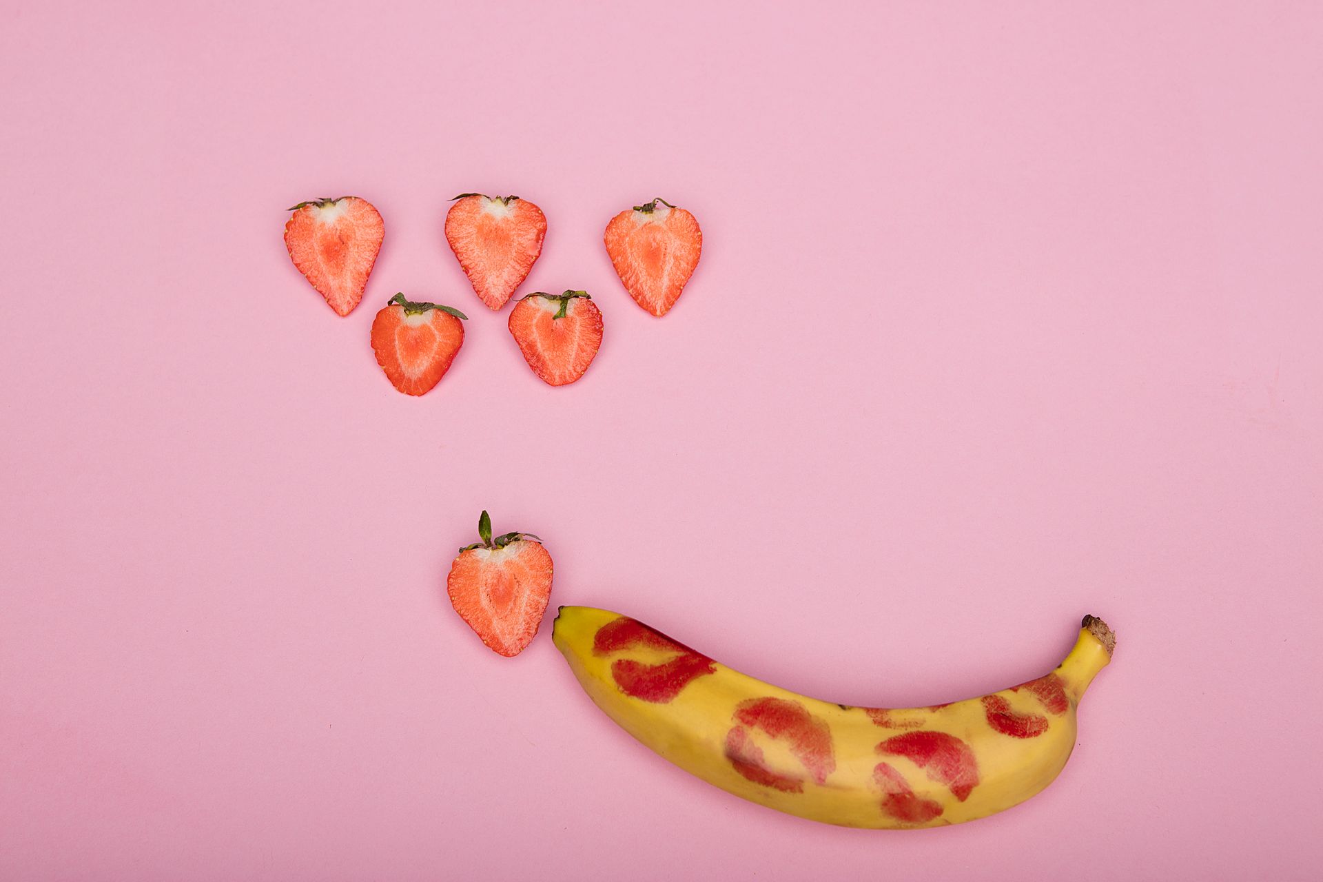 Creative conceptual display using bananas, strawberries on pink background, symbolizing sexuality and romance.