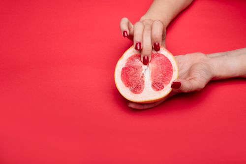 Free Close-up view of a hand with red nails holding a grapefruit against a red background. Symbolic and abstract. Stock Photo