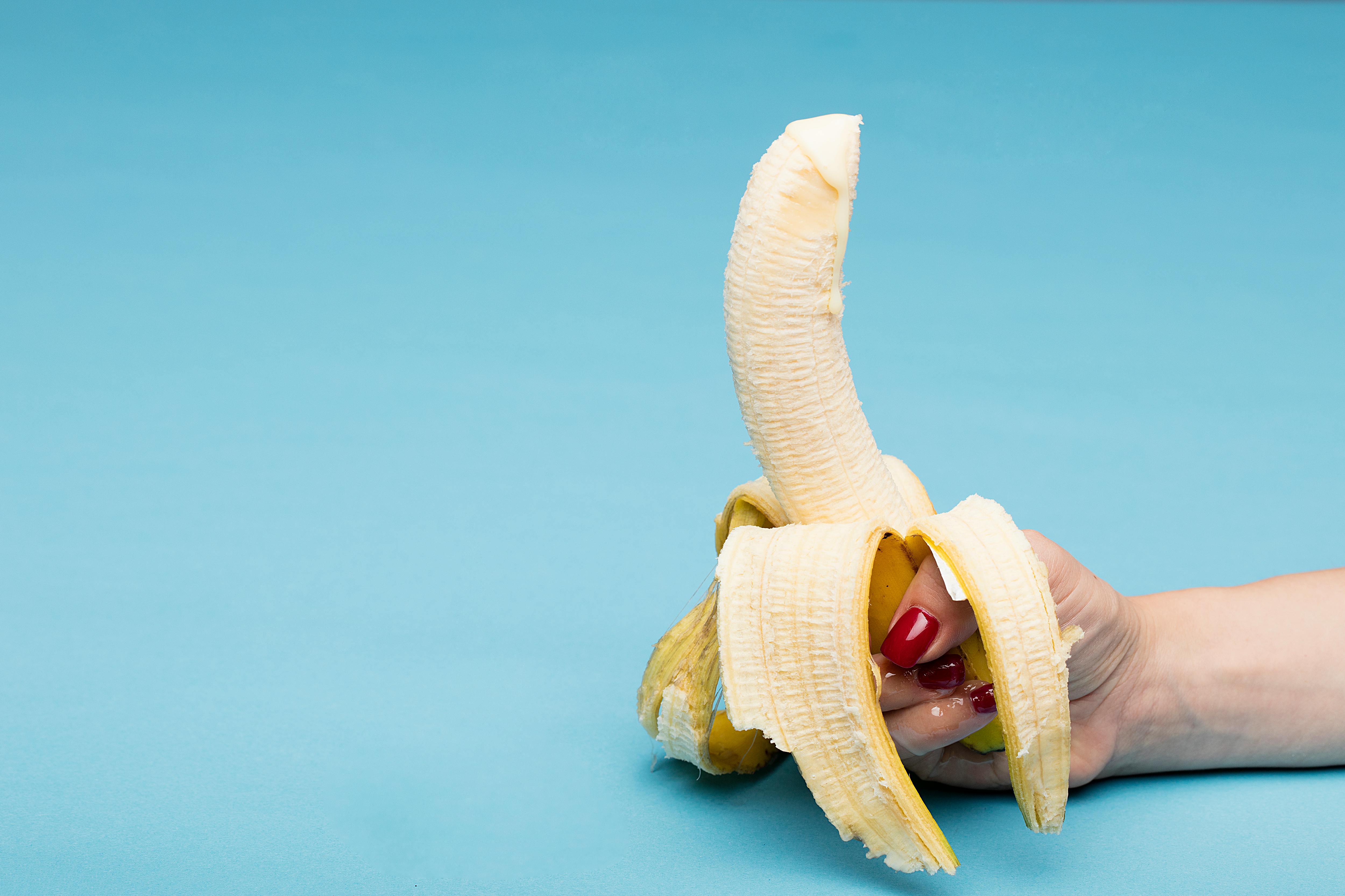 A close-up of a hand holding a peeled banana with a vibrant blue background, composition ideal for food photography.