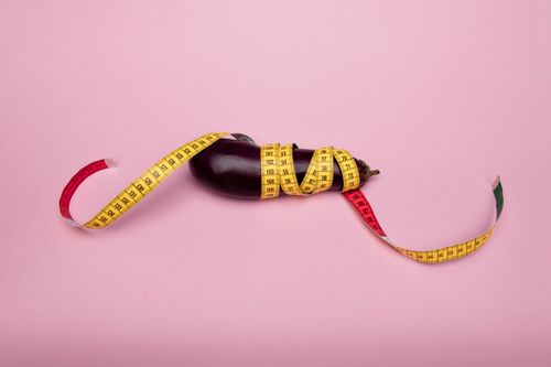 Free A humorous concept with an eggplant wrapped in a tape measure on a pink background. Stock Photo