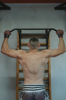 Strong shirtless man doing pull-ups in the gym, showcasing fit and muscular physique.
