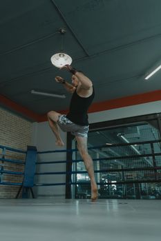 A male boxer leaps midair in a boxing ring during training, showcasing athletic prowess.