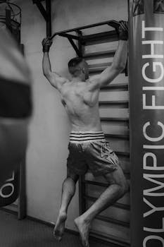A muscular man performs pull-ups in a gym, emphasizing strength and fitness.