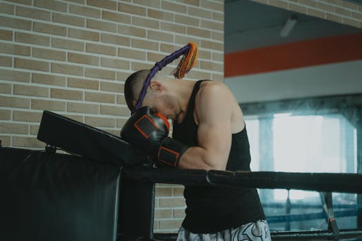 A boxer wearing traditional headgear rests in the corner of a boxing ring, reflecting on the match.